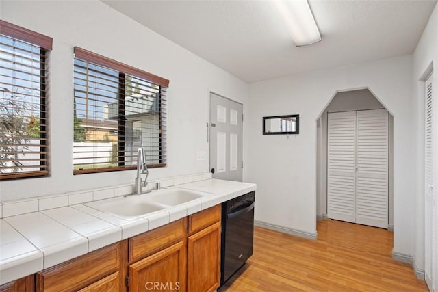 kitchen featuring black dishwasher, brown cabinets, light wood finished floors, tile counters, and a sink