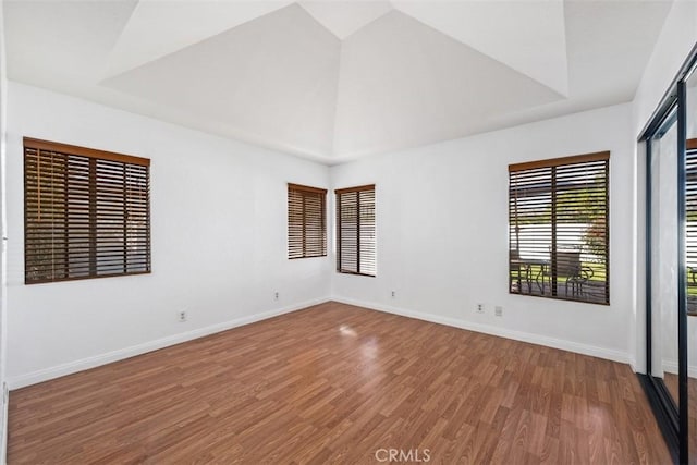 unfurnished room featuring high vaulted ceiling, baseboards, and wood finished floors