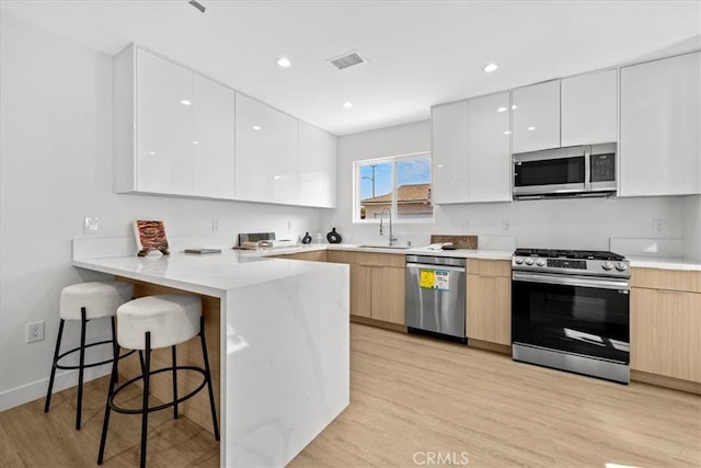 kitchen featuring stainless steel appliances, a peninsula, a sink, a kitchen breakfast bar, and modern cabinets