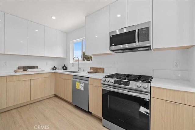 kitchen featuring modern cabinets, appliances with stainless steel finishes, light countertops, light brown cabinets, and a sink