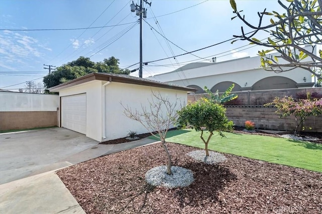 view of yard with a garage, fence, concrete driveway, and an outbuilding