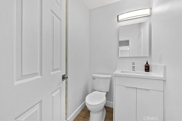 bathroom featuring toilet, baseboards, wood finished floors, and vanity