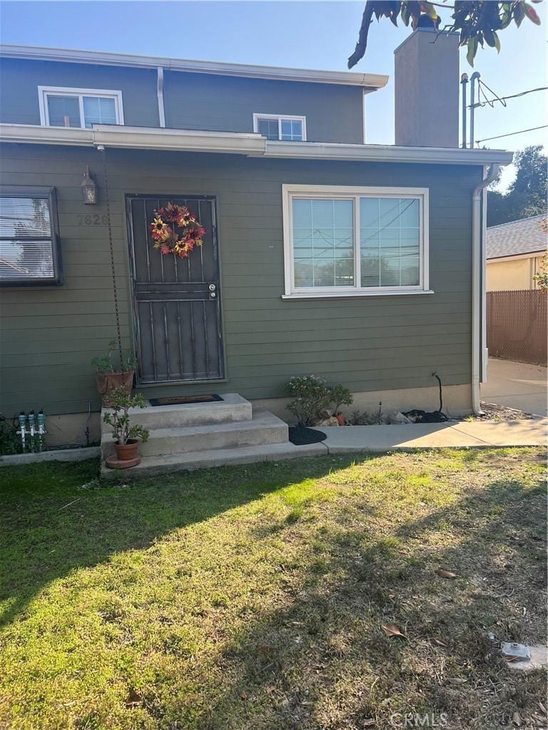 view of exterior entry with a lawn, a chimney, and fence