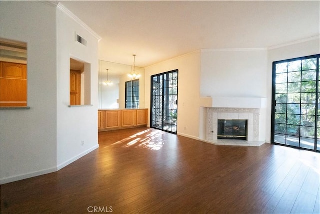 unfurnished living room featuring crown molding, wood finished floors, a wealth of natural light, and an inviting chandelier