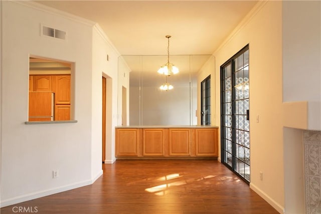 unfurnished dining area featuring baseboards, visible vents, wood finished floors, crown molding, and a chandelier