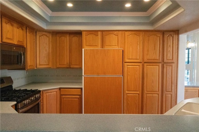 kitchen with stainless steel gas range oven, refrigerator, light countertops, a tray ceiling, and crown molding