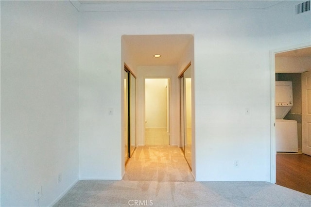 hallway featuring stacked washer / dryer, carpet, and visible vents