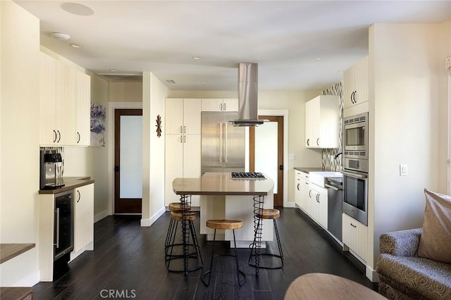 kitchen with a breakfast bar area, appliances with stainless steel finishes, dark wood-style floors, dark countertops, and island exhaust hood