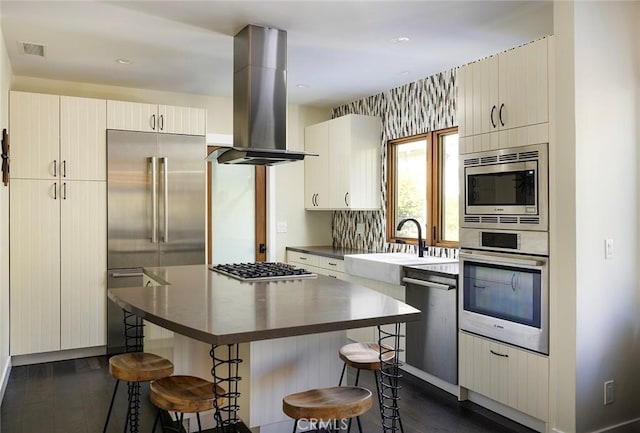 kitchen featuring built in appliances, island range hood, a sink, a kitchen breakfast bar, and dark countertops