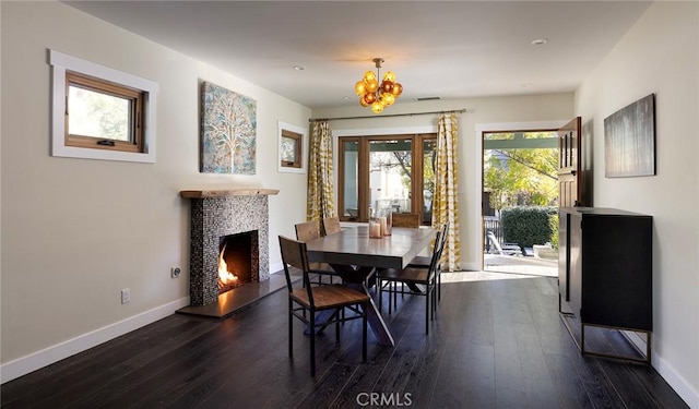 dining room featuring dark wood-type flooring, a warm lit fireplace, and baseboards