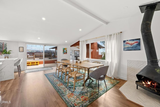 dining area with lofted ceiling with beams, wood finished floors, a wood stove, and a healthy amount of sunlight