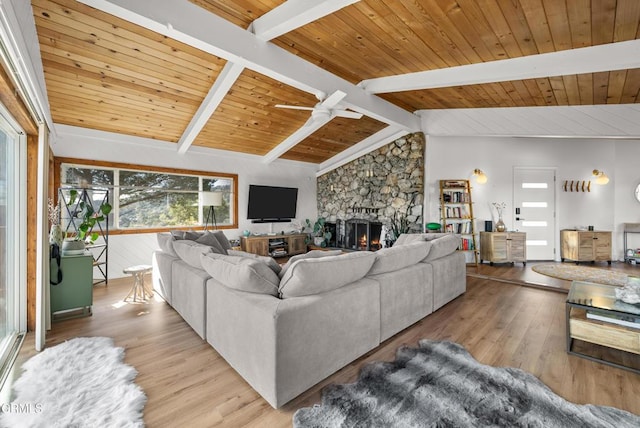 living room with vaulted ceiling with beams, ceiling fan, a stone fireplace, wood finished floors, and wood ceiling