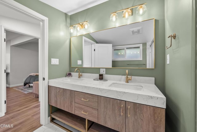 ensuite bathroom featuring double vanity, visible vents, a sink, and wood finished floors