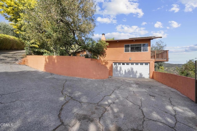 view of front of home featuring aphalt driveway, a garage, fence, stucco siding, and a chimney