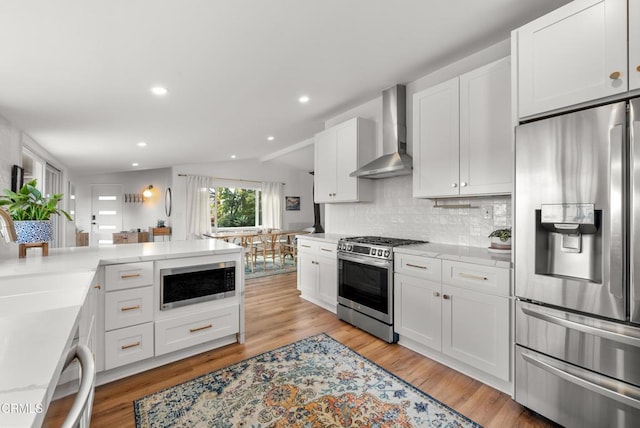 kitchen with lofted ceiling, wall chimney exhaust hood, appliances with stainless steel finishes, and light wood-style flooring