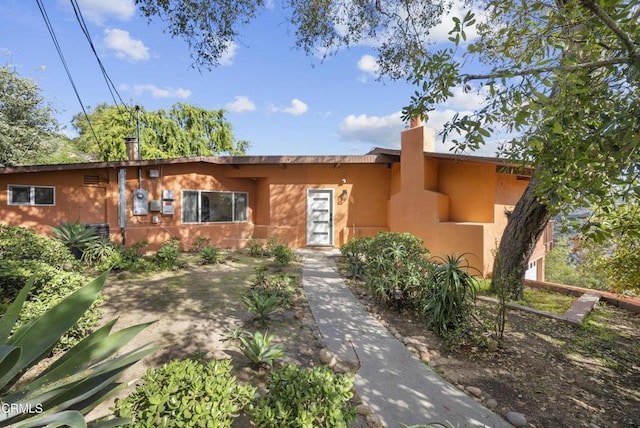 pueblo revival-style home featuring a chimney and stucco siding