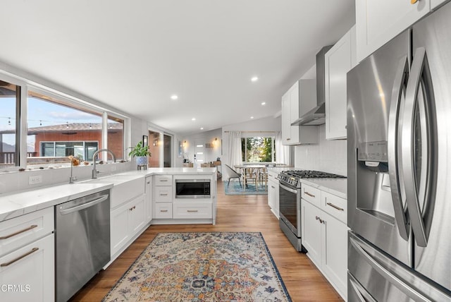 kitchen with stainless steel appliances, wall chimney exhaust hood, white cabinets, and light wood finished floors