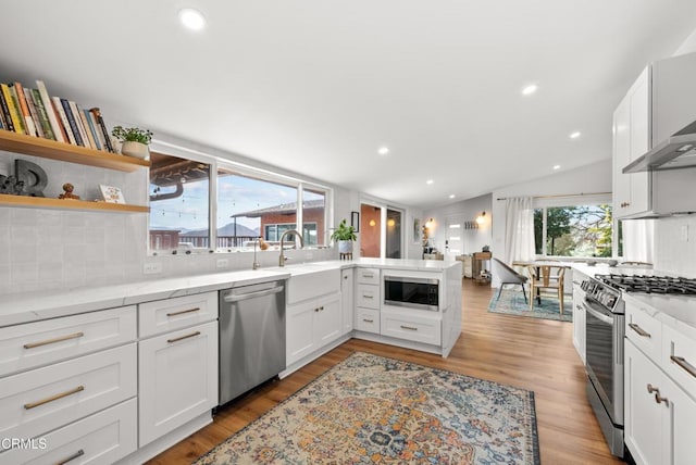 kitchen with light wood finished floors, tasteful backsplash, appliances with stainless steel finishes, a sink, and a peninsula