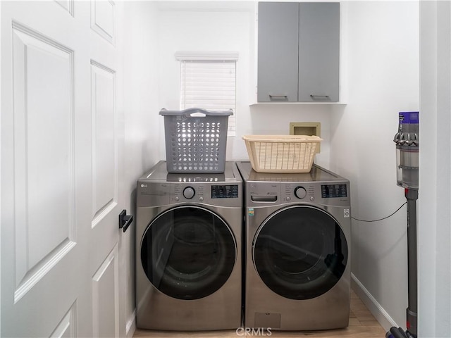 clothes washing area featuring cabinet space, baseboards, wood finished floors, and washing machine and clothes dryer