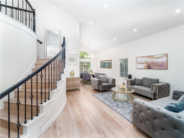 living room with stairs, high vaulted ceiling, light wood finished floors, and a chandelier