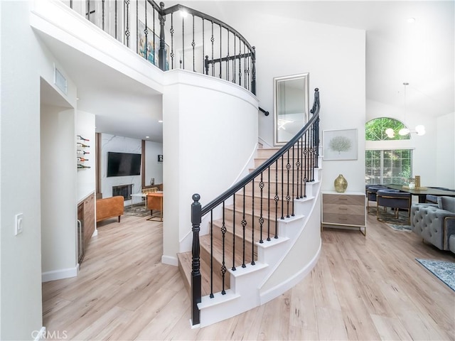 stairs featuring a fireplace, wood finished floors, a towering ceiling, and a notable chandelier