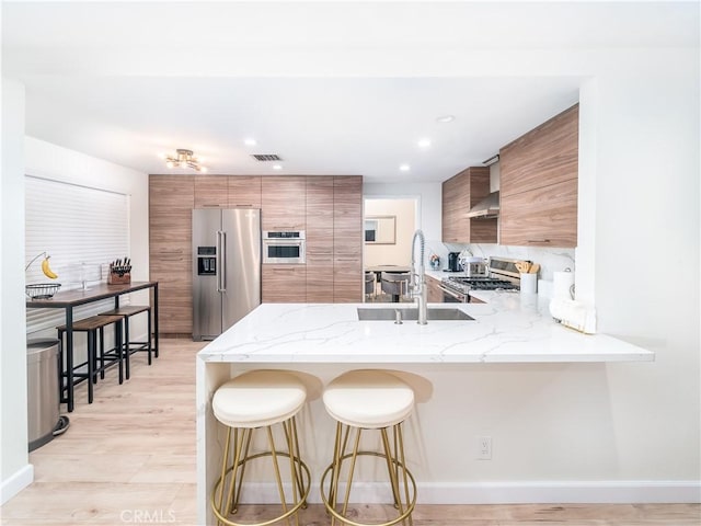 kitchen featuring a breakfast bar area, a peninsula, visible vents, appliances with stainless steel finishes, and brown cabinets