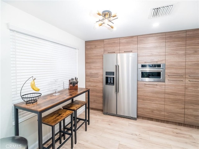 kitchen with appliances with stainless steel finishes, visible vents, and brown cabinets