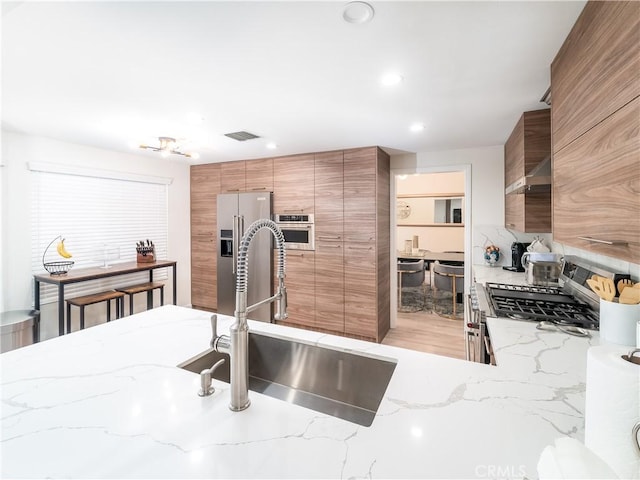 kitchen featuring visible vents, modern cabinets, appliances with stainless steel finishes, brown cabinets, and a sink