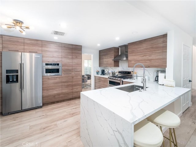 kitchen featuring visible vents, appliances with stainless steel finishes, light stone counters, wall chimney range hood, and a sink