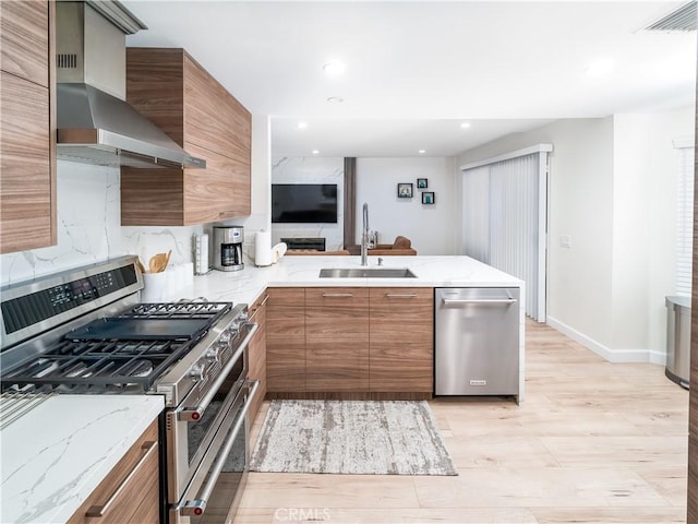 kitchen featuring visible vents, brown cabinetry, stainless steel appliances, wall chimney range hood, and a sink