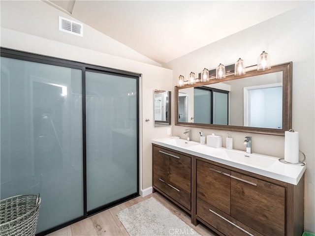 full bathroom featuring lofted ceiling, wood finished floors, a sink, visible vents, and double vanity