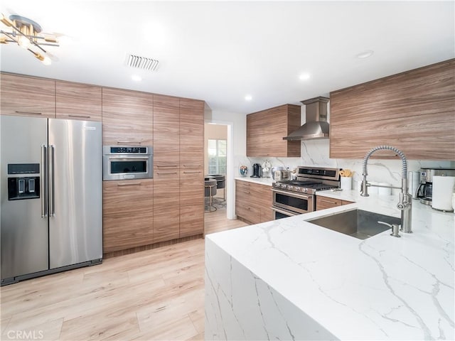 kitchen featuring premium appliances, light stone countertops, a sink, modern cabinets, and wall chimney exhaust hood