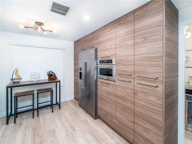 kitchen with light wood finished floors, visible vents, modern cabinets, and appliances with stainless steel finishes