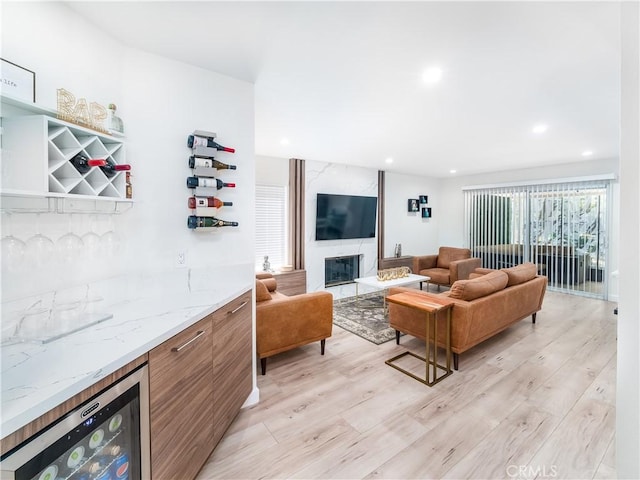 living area featuring wine cooler, recessed lighting, a fireplace, light wood-type flooring, and a dry bar