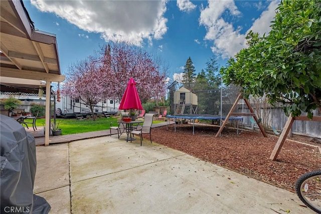 view of patio with a trampoline, a playground, a fenced backyard, and grilling area