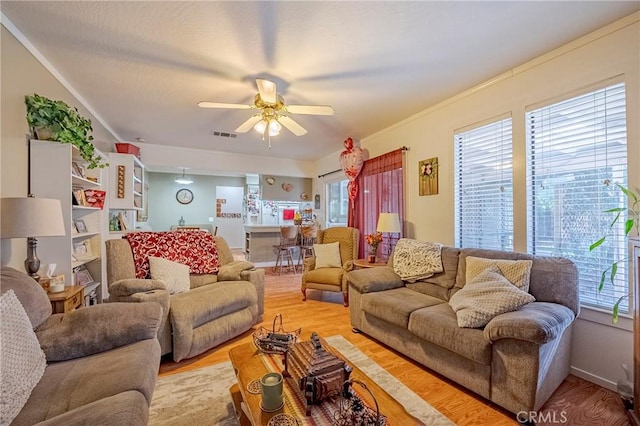 living room featuring crown molding, visible vents, light wood-style floors, ceiling fan, and baseboards