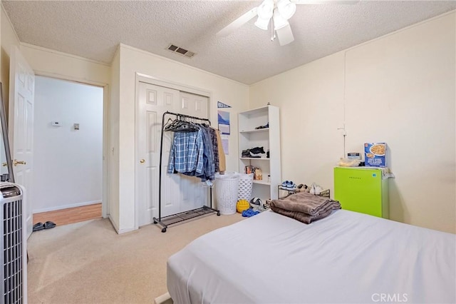 carpeted bedroom with visible vents, ceiling fan, heating unit, a textured ceiling, and a closet