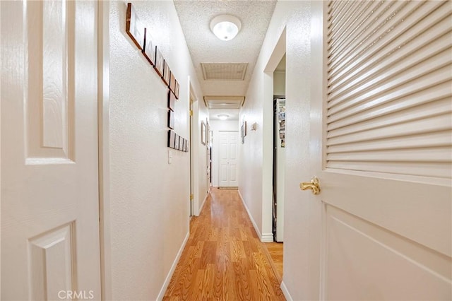 corridor with a textured ceiling, light wood finished floors, visible vents, and baseboards