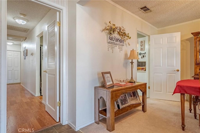 corridor featuring ornamental molding, visible vents, a textured ceiling, and baseboards