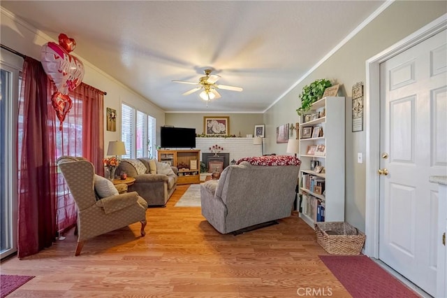 living area featuring light wood finished floors, ceiling fan, a fireplace, and crown molding