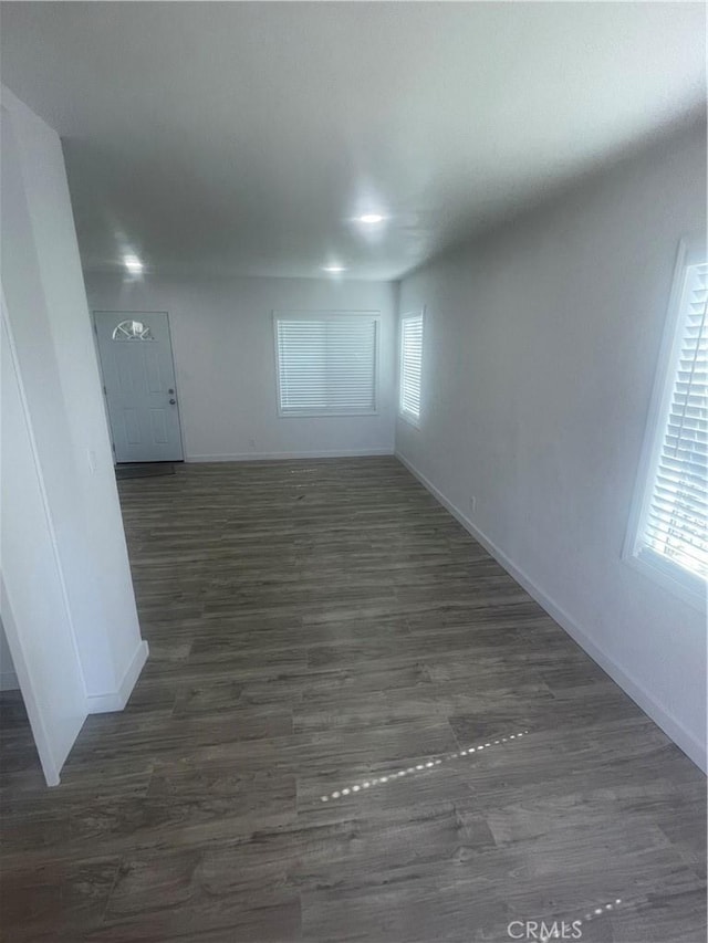 unfurnished room with a wealth of natural light, baseboards, and dark wood-style flooring