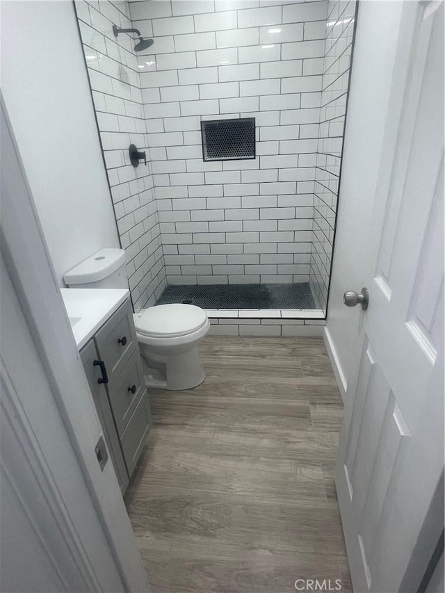 bathroom featuring visible vents, toilet, wood finished floors, a tile shower, and vanity