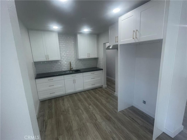 kitchen with white cabinets, decorative backsplash, dark countertops, dark wood-style flooring, and a sink