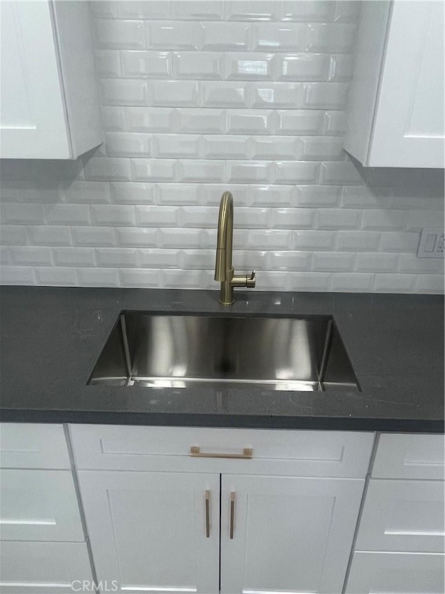 kitchen featuring dark countertops, white cabinetry, decorative backsplash, and a sink