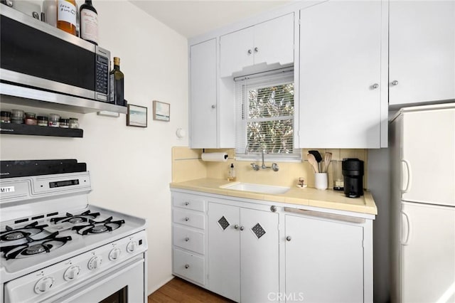 kitchen with light countertops, white appliances, a sink, and white cabinetry