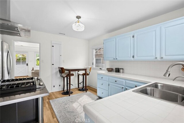 kitchen with tile countertops, backsplash, freestanding refrigerator, a sink, and blue cabinets