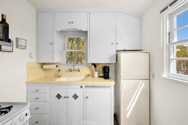 kitchen featuring a sink, freestanding refrigerator, and white cabinetry