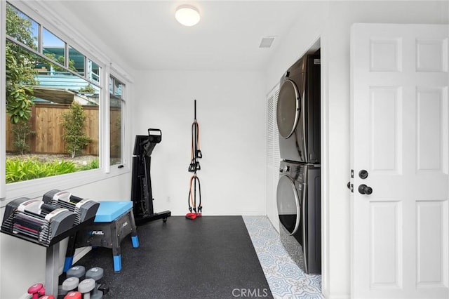 exercise area with visible vents, stacked washer and clothes dryer, and baseboards