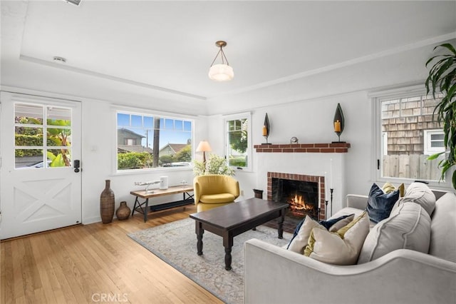 living room featuring a brick fireplace, wood-type flooring, and a tray ceiling