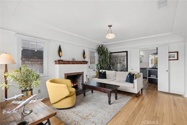 living room featuring light wood-style floors, a brick fireplace, and visible vents